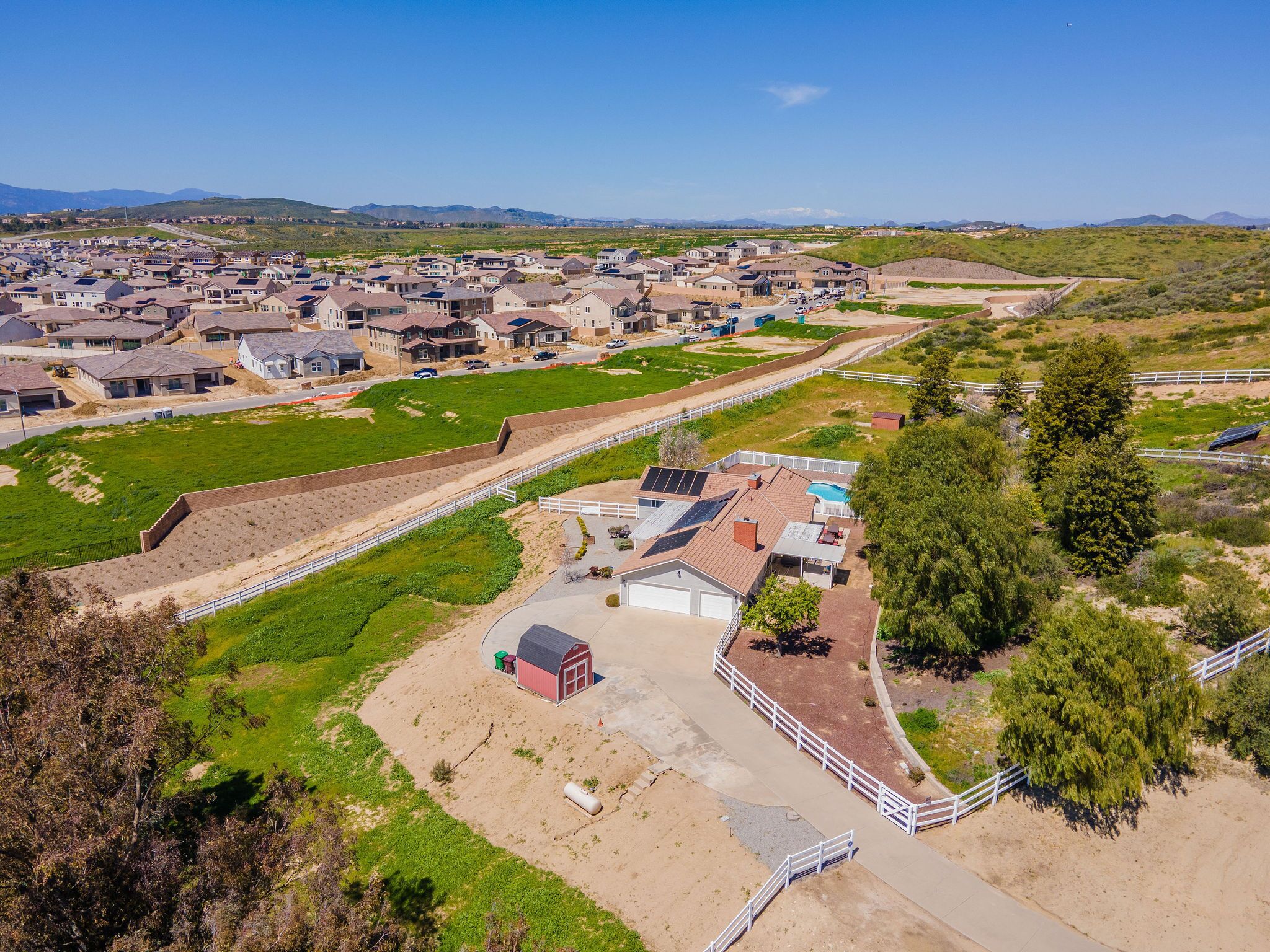 An aerial view of a residential area with houses, a fenced sports field, and a small building with a red roof.