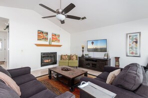 A living room with a fireplace, a ceiling fan, and a television.