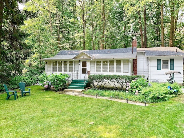Ein weißes Haus mit Veranda, grünen Stufen und einem kleinen Garten mit Rasen und Sträuchern.