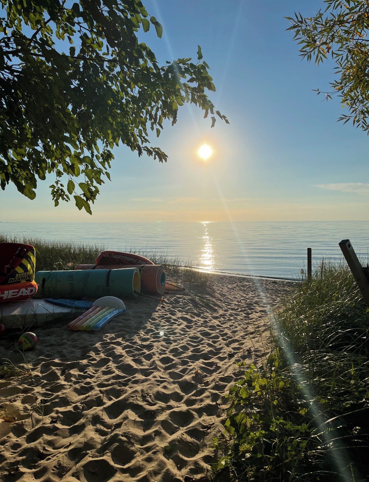 Une plage avec un ciel dégagé, le soleil se couchant ou se levant, et du matériel de plage comme une planche de surf et une planche de bodyboard.