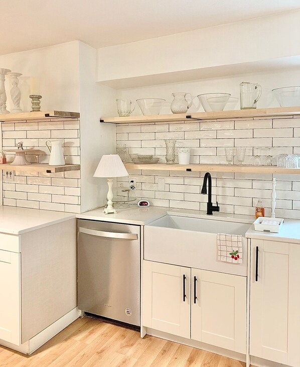 A modern kitchen with white cabinetry, a stainless steel dishwasher, and a tiled backsplash. - Cozy Lakeside Cottage.... with access to a private beach! (Lakeside)