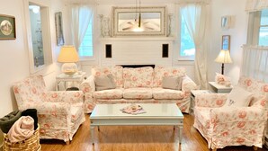 A cozy living room with a floral sofa set, a glass coffee table, and a fireplace.
