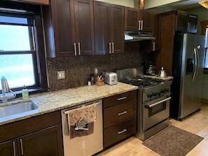 A kitchen with dark wood cabinets, a granite countertop, stainless steel appliances, and a window with a view.