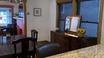 A kitchen with granite countertops, wooden cabinets, a dining area with chairs, and a hanging pendant light.