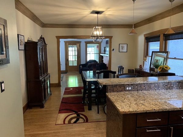 A kitchen with a granite countertop, wooden cabinets, a dining area with chairs, and a hallway leading to another room.