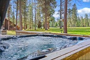 Een hottub omringd door een houten terras, met een bebost gebied op de achtergrond.
