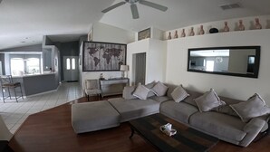 A modern living room with a sectional sofa, a coffee table, and a dining area with a bar. - WOW! Championsgate-Minutes to disney,private pool,wifi ,tennis,gym,games room  (Davenport)