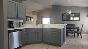 A modern kitchen with grey cabinets, a dishwasher, a coffee maker, and a dining area with a table and chairs. - WOW! Championsgate-Minutes to disney,private pool,wifi ,tennis,gym,games room  (Davenport)