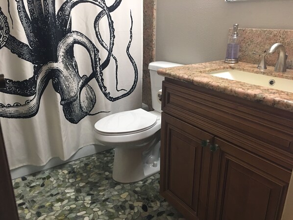 A bathroom with a mosaic floor, a toilet, a sink with a faucet, and a cabinet. - Harbor House in Morro Bay (Morro Bay)
