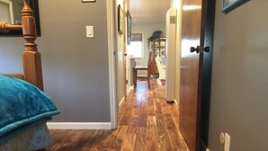 A hallway with wooden flooring, a bed with a blue cover, and a door leading to another room. - Harbor House in Morro Bay  (Morro Bay)
