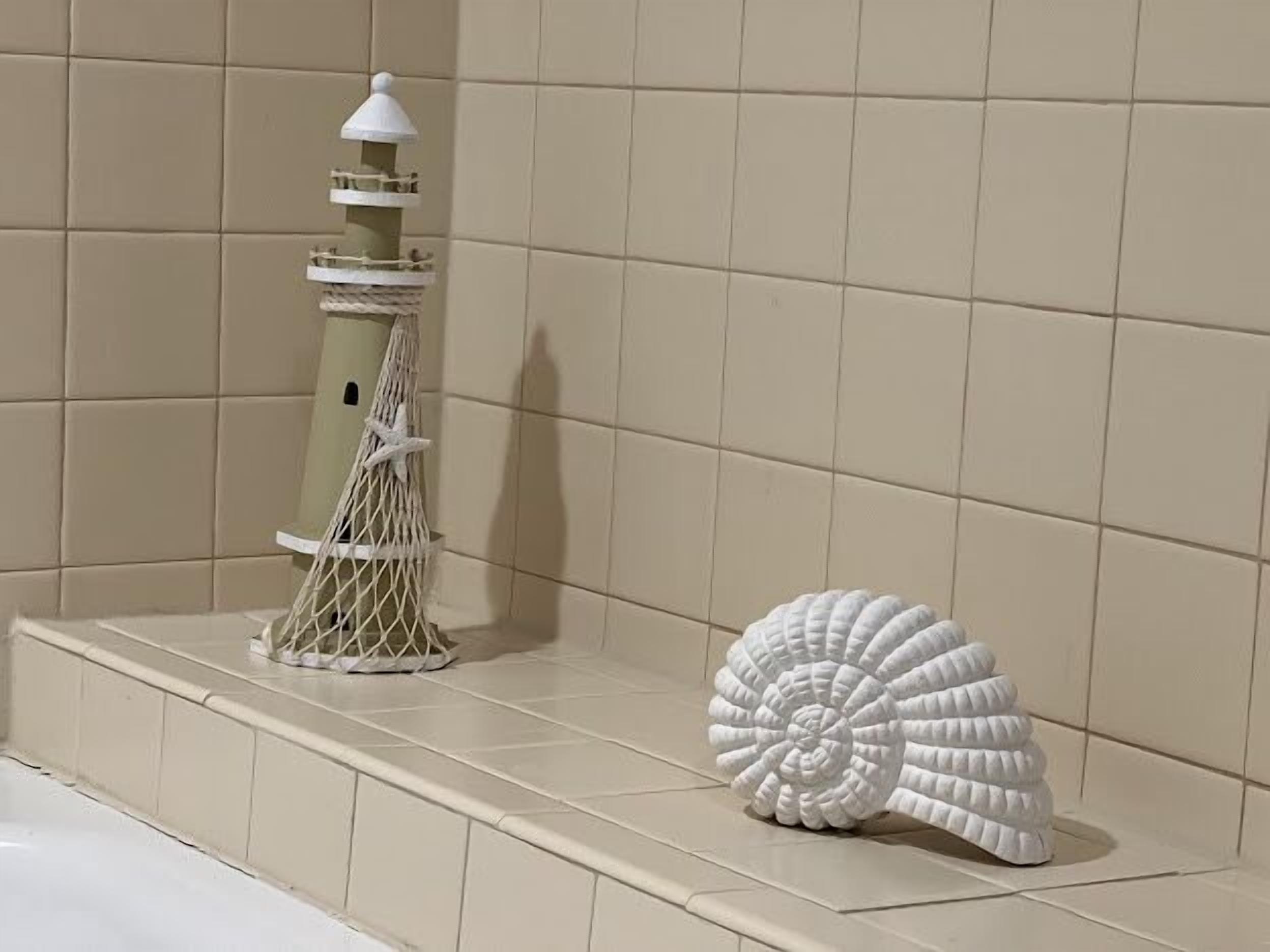 Een badkamer met beige tegels, een witte decoratieve vuurtoren en een schelp op de rand.