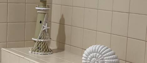 Een badkamer met beige tegels, een witte decoratieve vuurtoren en een schelp op de rand.
