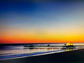 Un atardecer sobre una playa con un muelle que se adentra en el agua.