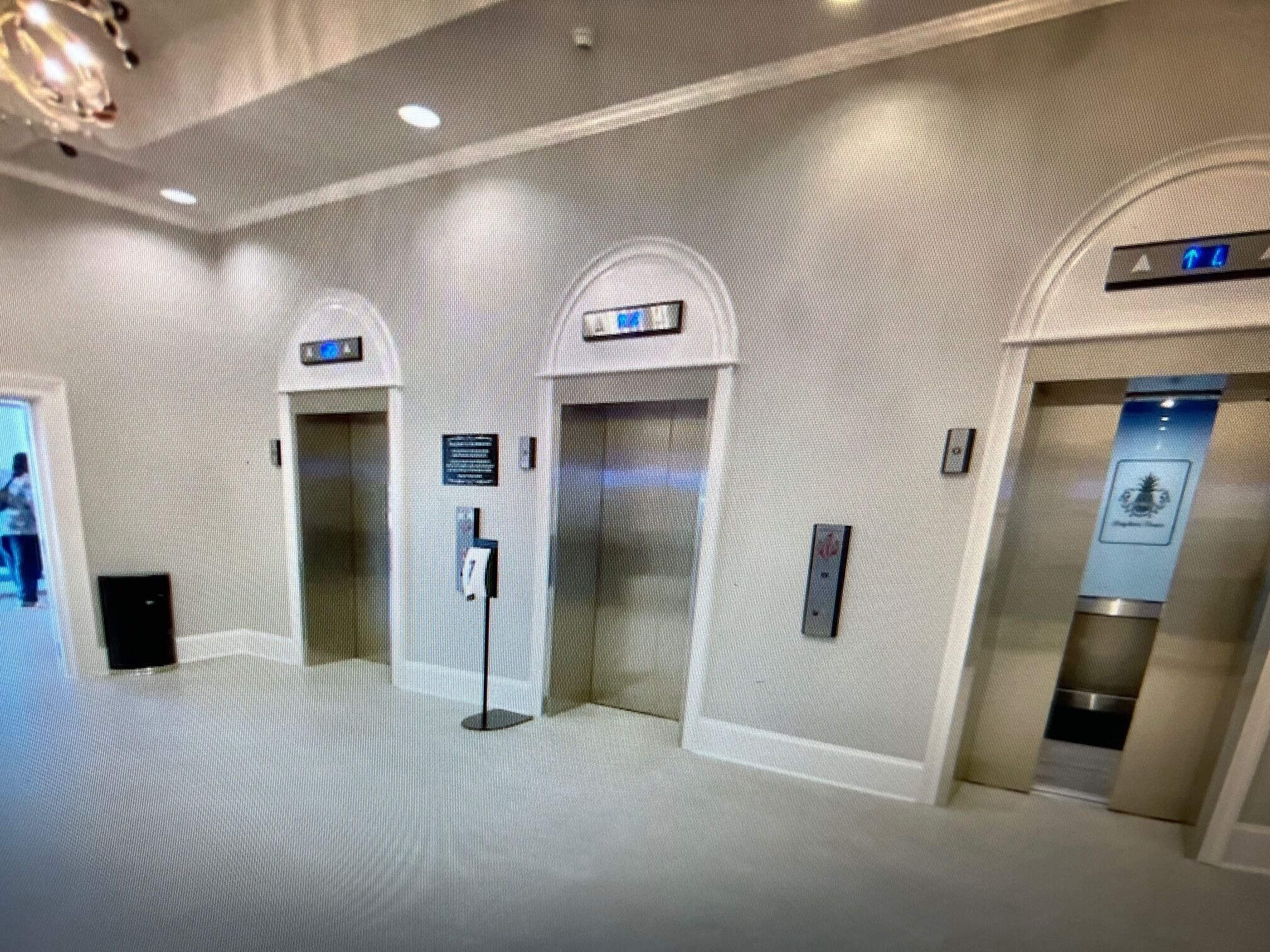 A modern elevator area with two elevators, a digital display, and a sign indicating the direction of travel.