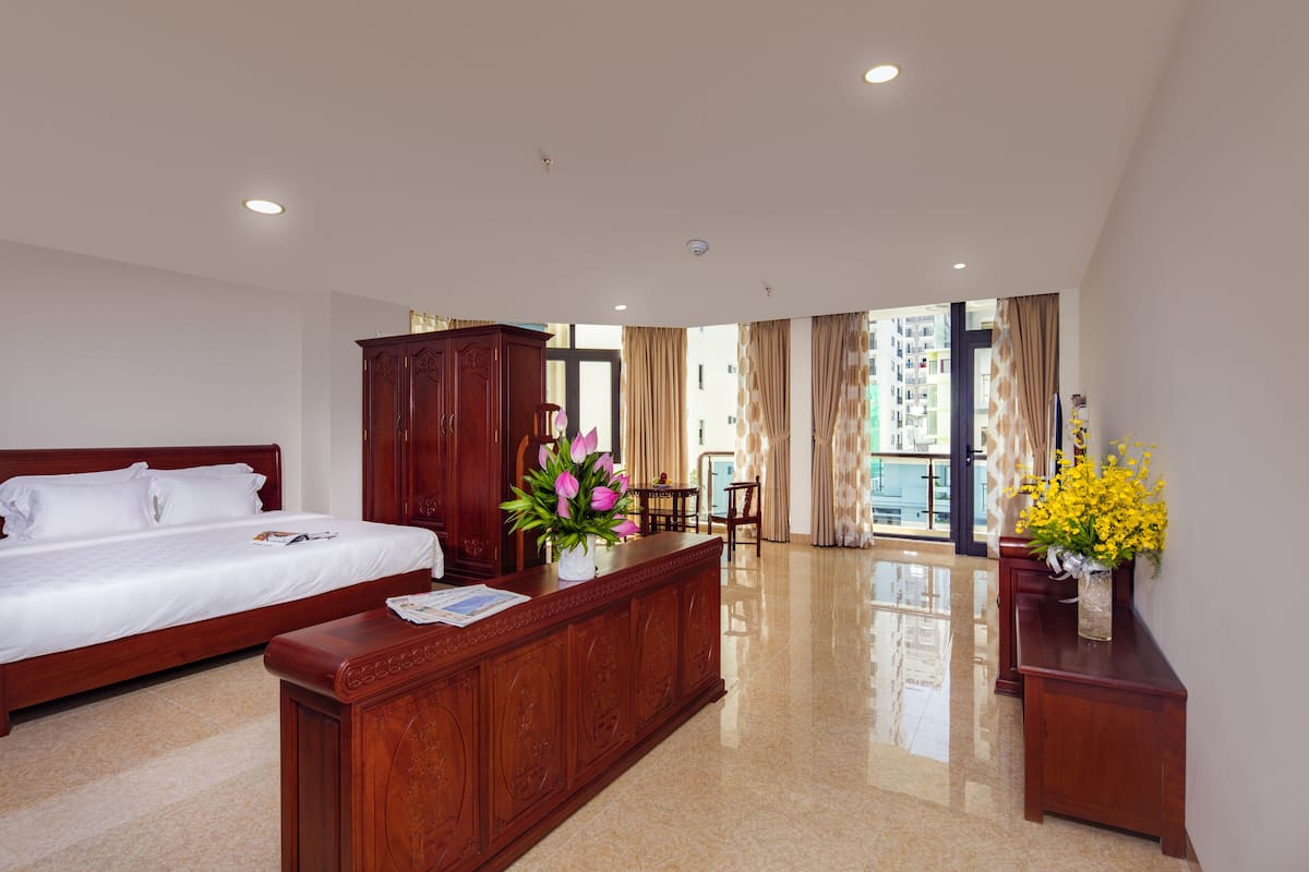 Quarto de hotel com cama, escrivaninha de madeira, uma cadeira e vista para o exterior.