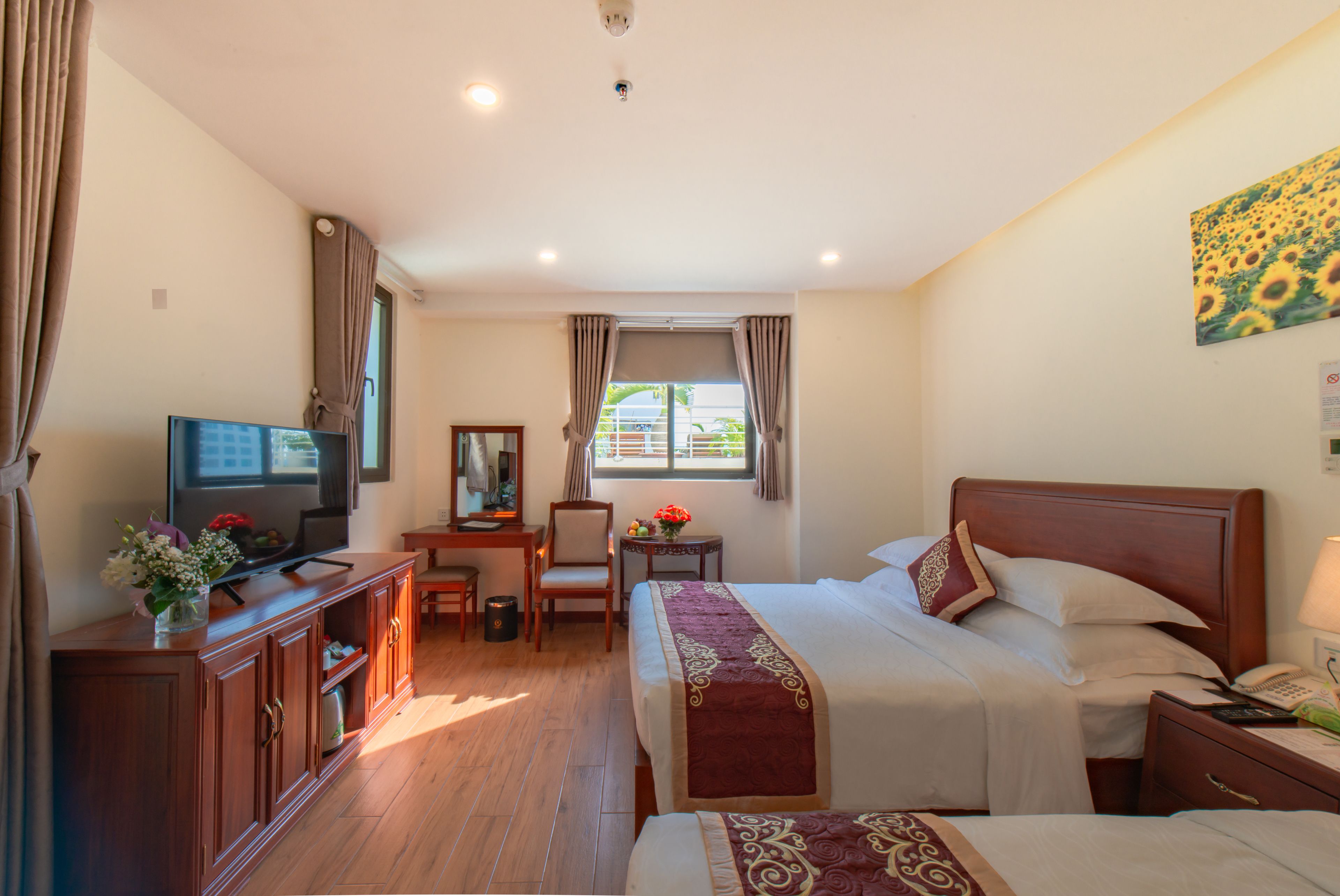 A hotel room with a bed, a desk with a chair, a television, a window with curtains, and a painting on the wall.