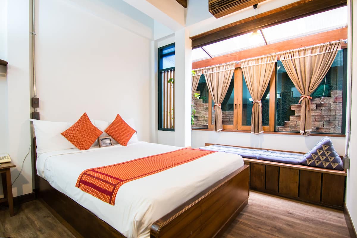 A bedroom with a large bed, a wooden bench, and a window with curtains.