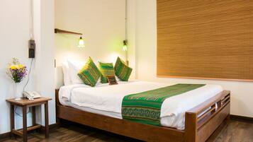 A neatly made bed with a green and white bedspread, a wooden bedside table with a phone, and a wall-mounted lamp.