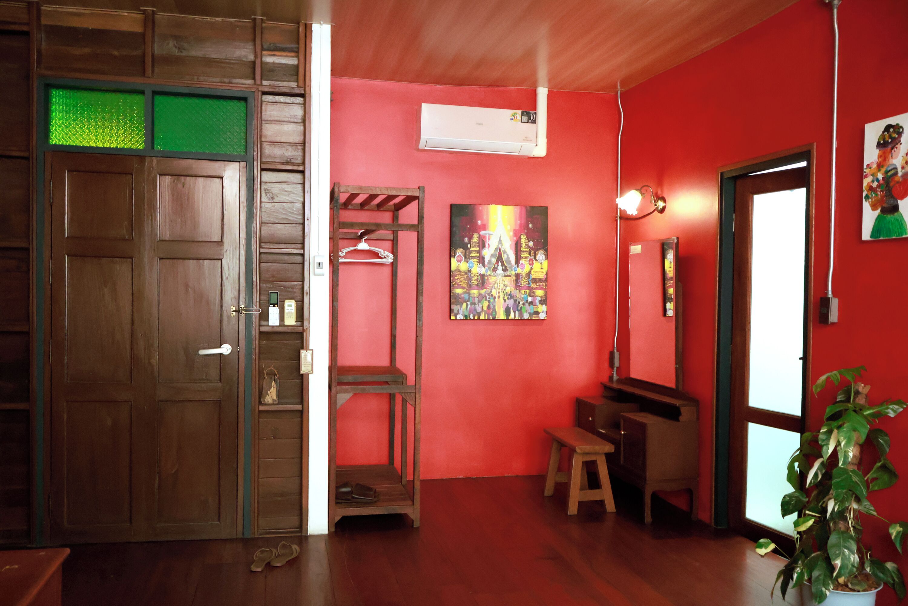 A room with a wooden door, a bench, a stool, a hanging rack, a wall-mounted air conditioner, and a potted plant.