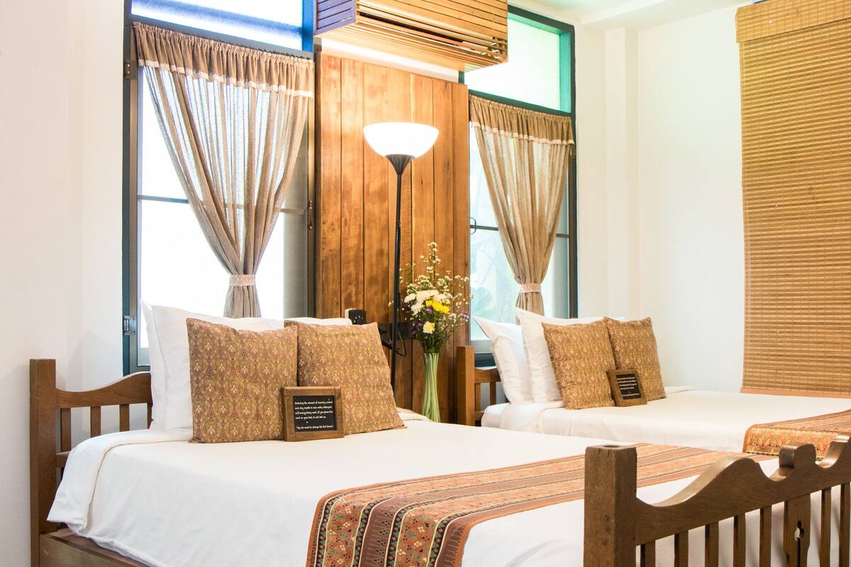 A double bed with a wooden frame, two bedside tables, a ceiling fan, and a large window with curtains.