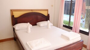 A neatly made bed with white linens and towels, a wooden headboard, and a window with curtains. - Chayta Resort (Rayong)
