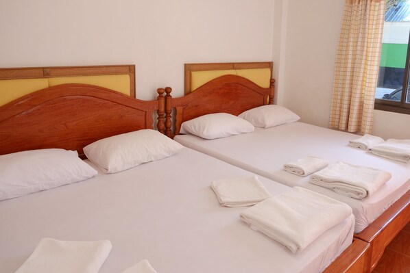 Dos camas individuales con cabeceras de madera, ropa de cama blanca y toallas ordenadamente dobladas.