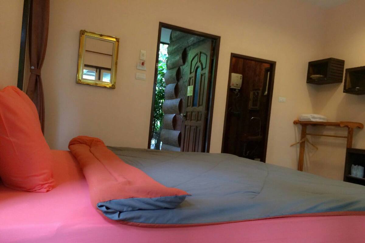 A bedroom with a bed, a mirror, a door, and a small shelf.