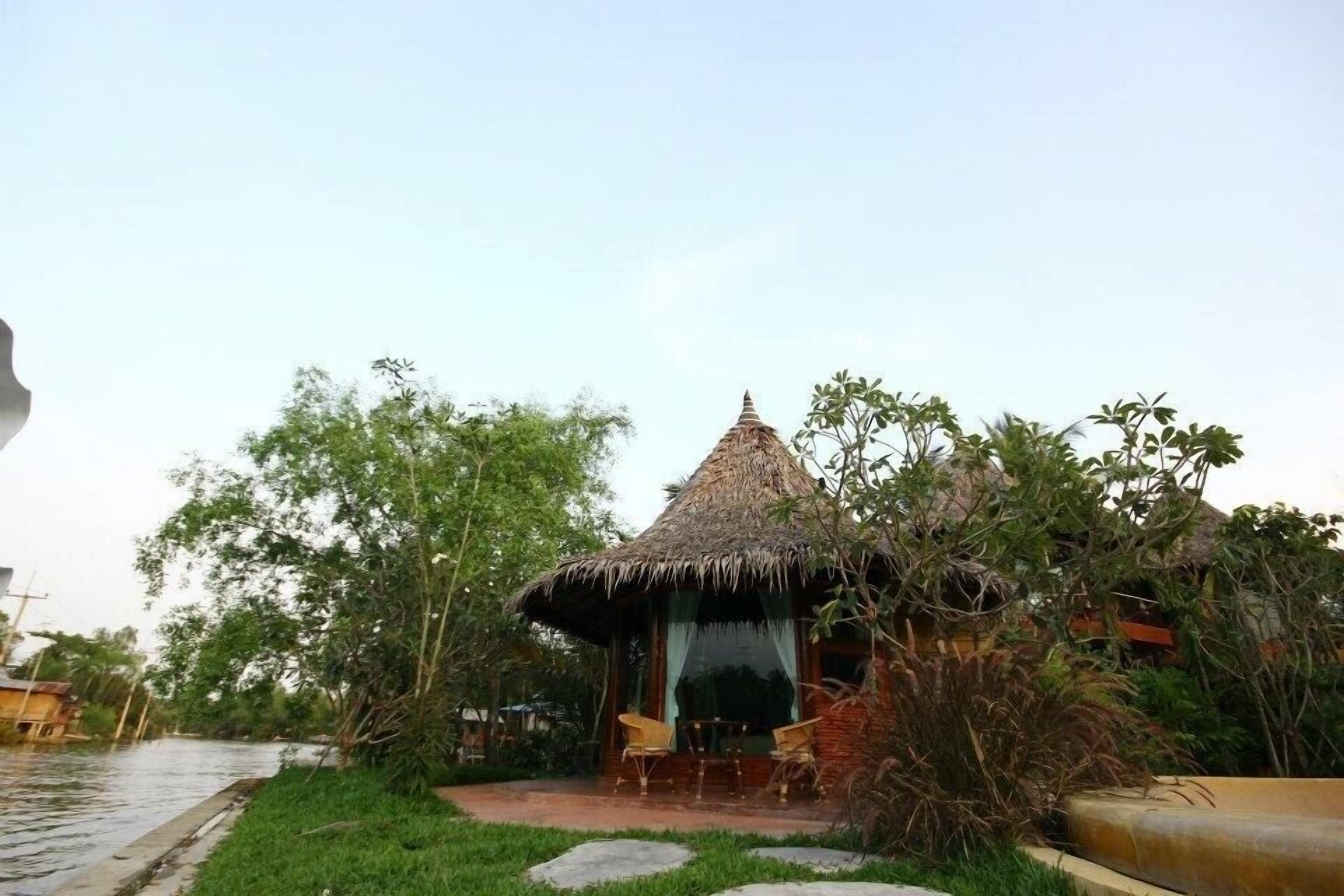 A thatched-roof hut with a small patio and two chairs.