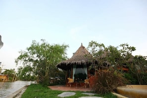 A thatched-roof hut with a small patio and two chairs. - Amphawa Club (Amphawa)