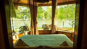 A room with a bed, two chairs, and a table, overlooking a body of water and greenery. - Amphawa Club (Amphawa)