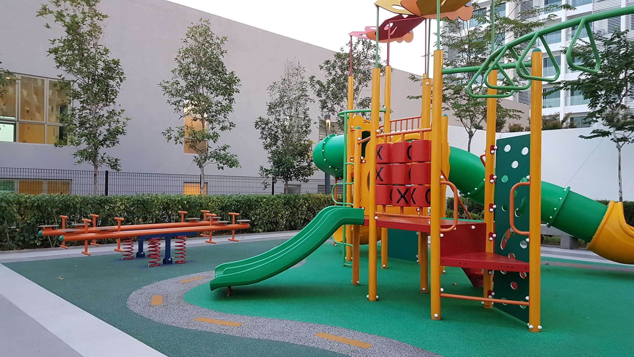 Une aire de jeux avec un toboggan et des structures d’escalade, entourée d’une zone pavée et d’arbres.