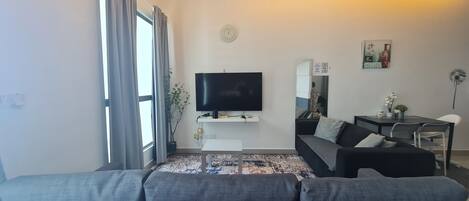A modern living room with a flat-screen TV, grey sofa, dining table, and chairs.