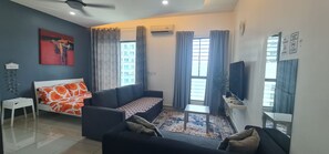 Ein modernes Wohnzimmer mit einer Couch, einem kleinen Tisch, einem Fernseher und einem Fenster mit Vorhängen.