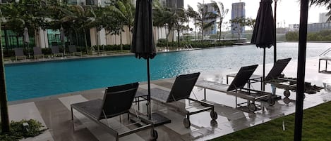 A poolside area with lounge chairs and umbrellas, a clear pool, and a modern building in the background.