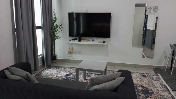 A living room with a sofa, a coffee table, a flat-screen TV mounted on the wall, a potted plant, and a large mirror. - Cyberjaya Cybersquare (Cyberjaya)