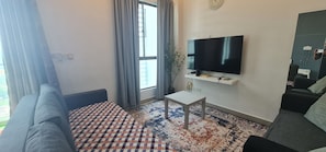 Ein Wohnzimmer mit einer Couch, einem an der Wand montierten Fernseher, einem kleinen Tisch und einem gemusterten Teppich.