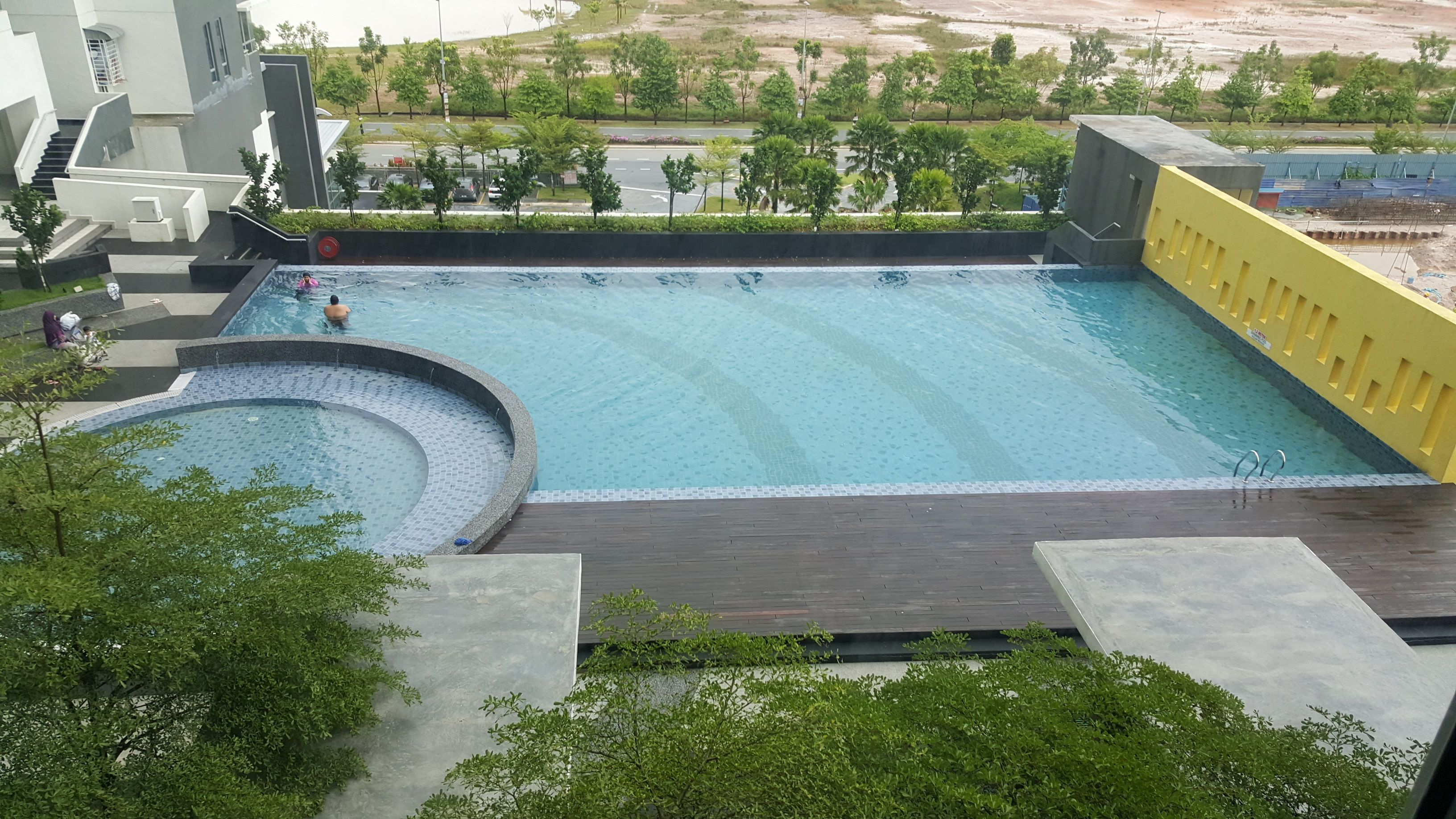 A large swimming pool with a circular section, surrounded by a deck and greenery.