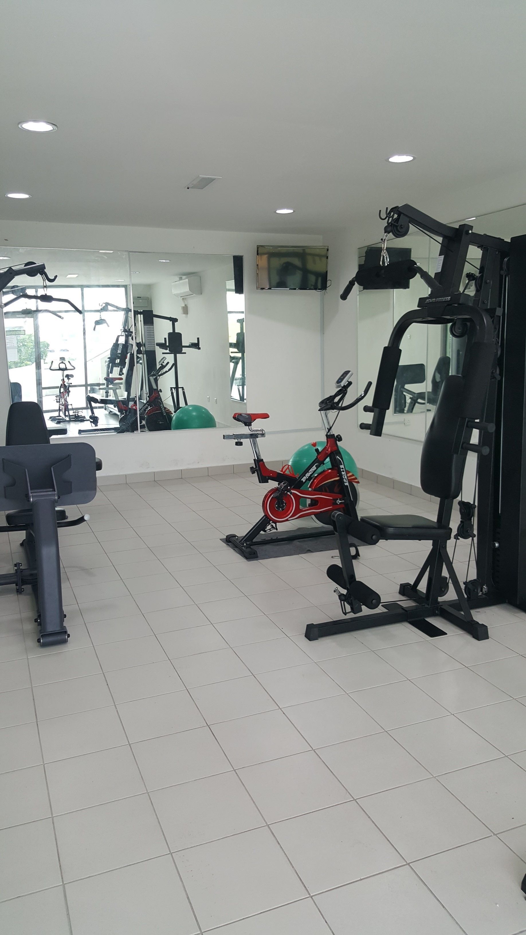 Een fitnessruimte met trainingsapparatuur, waaronder een hometrainer, een roeimachine en een gewichtbank.