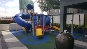 A playground with slides and climbing structures, surrounded by a paved area with blue and green patterns. - Cyberjaya Vega Residensi (Cyberjaya)