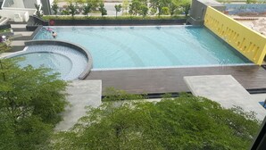 A large outdoor swimming pool with a circular hot tub area, surrounded by greenery and a yellow wall. - Cyberjaya Vega Residensi (Cyberjaya)