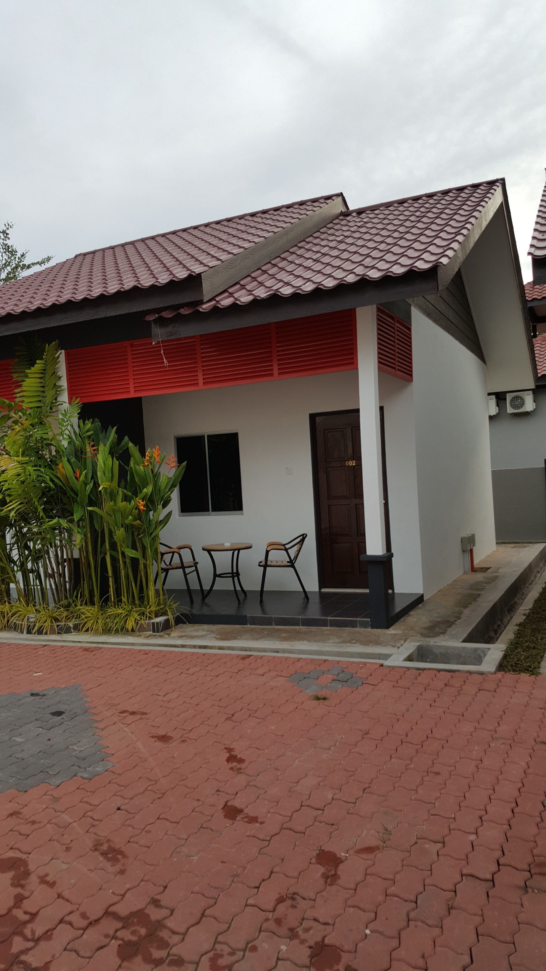 A modern house with a red roof, a small porch with two chairs, and a potted plant.