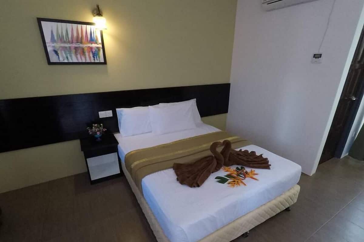 A hotel room with a bed, a nightstand, a wall-mounted lamp, and a door.