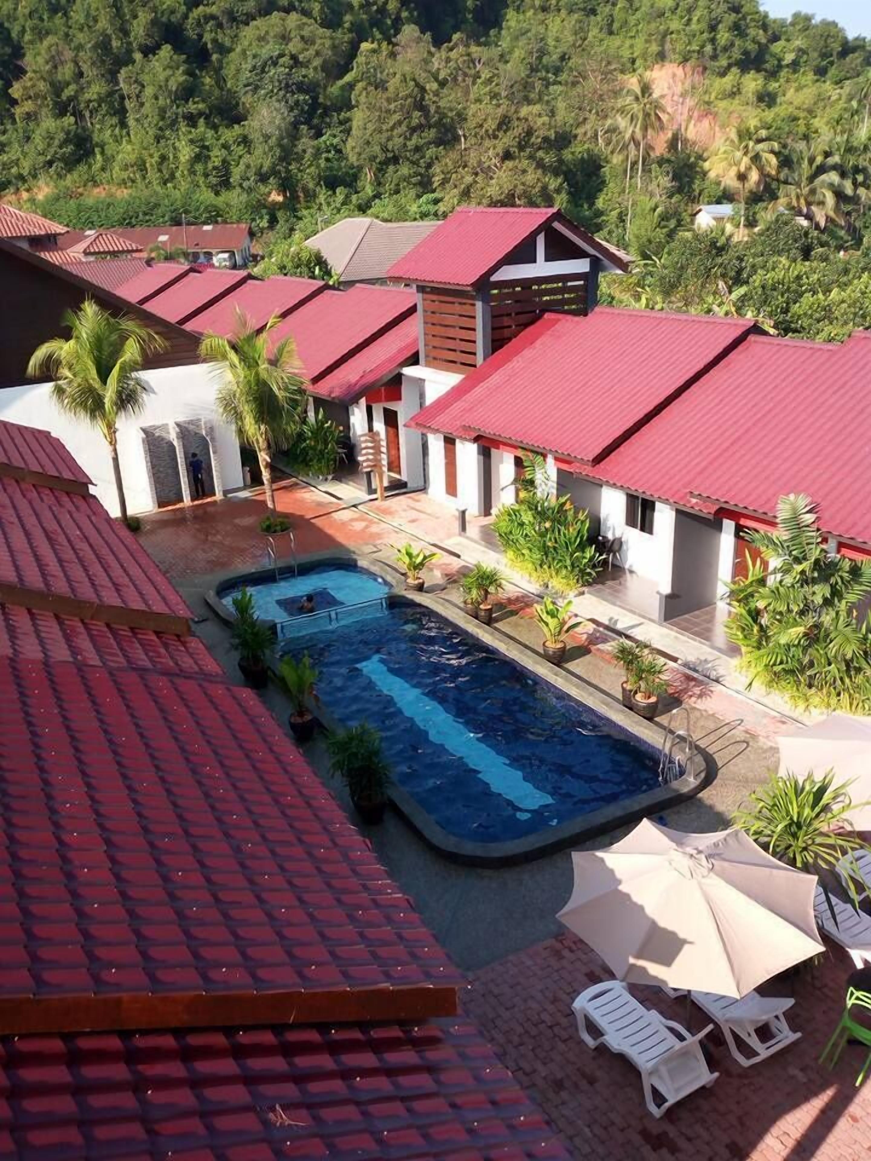 A resort with multiple buildings, a swimming pool, and lush greenery in the background.