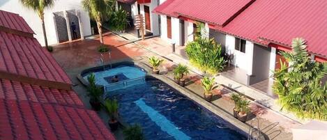 A resort with multiple buildings, a swimming pool, and lush greenery in the background.