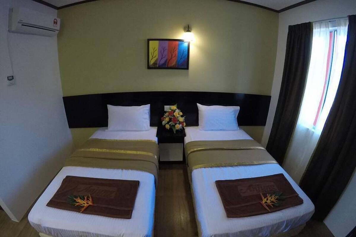 A hotel room with two beds, a nightstand with a vase of flowers, a painting on the wall, and an air conditioning unit.