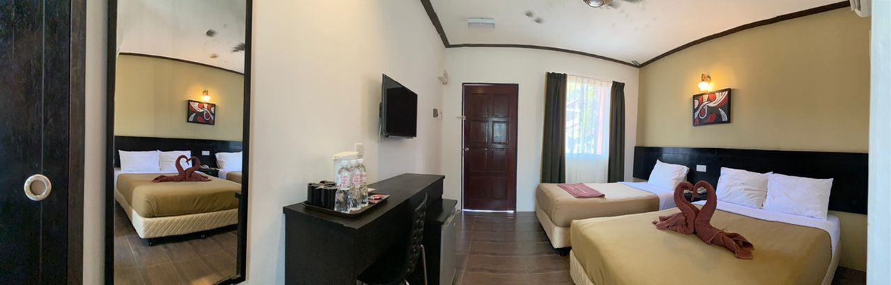 A hotel room with two beds, a desk with a mirror, a TV, and artwork on the walls.