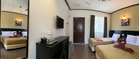 A hotel room with two beds, a desk with a mirror, a TV, and artwork on the walls.