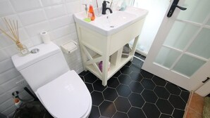 A bathroom with a white toilet, a white sink with toiletries, and a black hexagonal tiled floor.