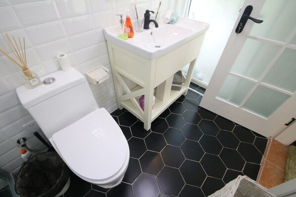 A bathroom with a white toilet, a white sink with toiletries, and a black hexagonal tiled floor. - Pushu Villa Shanghai NECC (Shanghai)