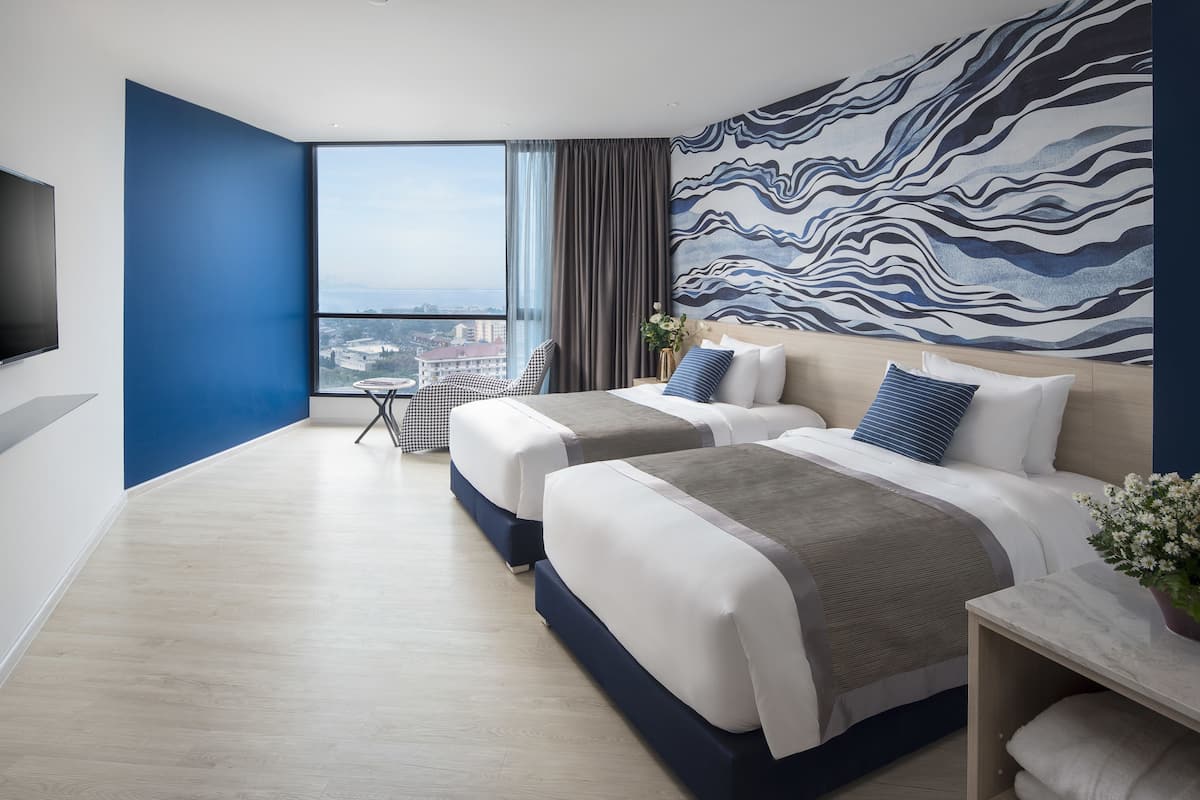 Ein modernes Hotelzimmer mit zwei Betten, einem großen Fenster mit Stadtblick, einem Flachbildfernseher und einer Wand mit Muster.